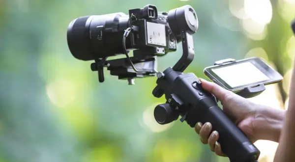 Ręka trzymająca stabilizator do kamery, czyli co to gimbal. Umożliwia płynne nagrywanie filmów.