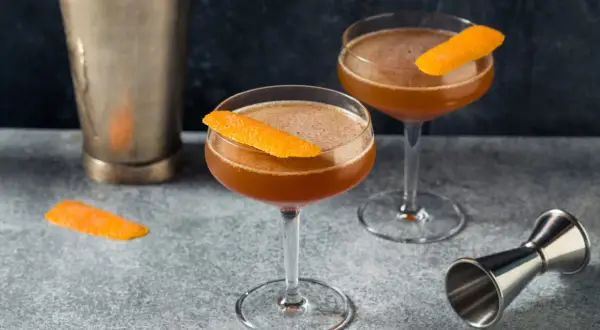 Zwei elegante Cocktails, garniert mit Orangenschale, stehen bereit. Ein "Blood and Sand Cocktail" wartet auf seinen Genuss.