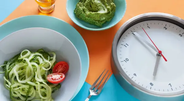 Zegar pokazuje 12:55. Czy kawa kuloodporna przerywa post? Obok talerz z cukinią i pomidorkami, miseczka z zielonym pesto i oliwa.