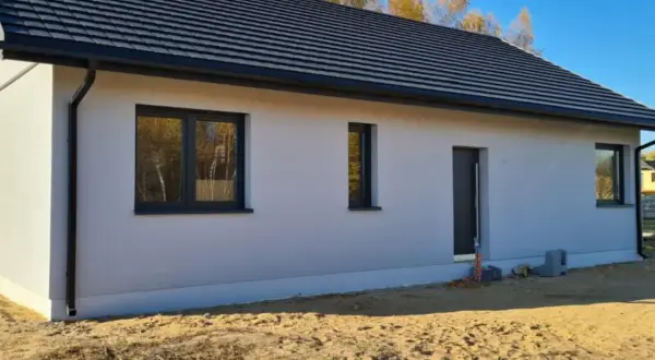 Nowy dom w stanie surowym zamkniętym z szarym dachem i oknami, otoczony piaskiem.
