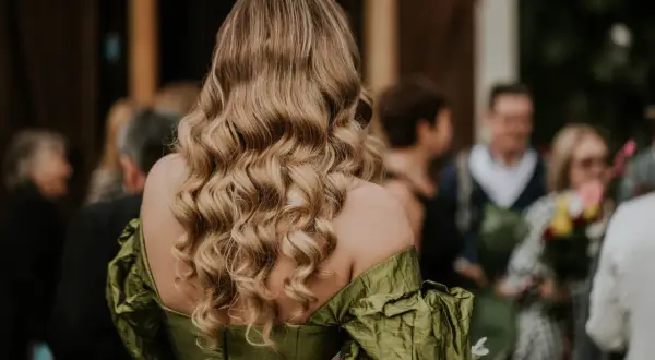 Eleganckie, falowane włosy blond to idealne fryzury na wesele jako gość. Widać je na tle innych weselników.