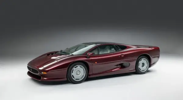 Bordowy Jaguar XJ220, ikona lat 90., prezentuje swoje aerodynamiczne linie na tle szarego studia.