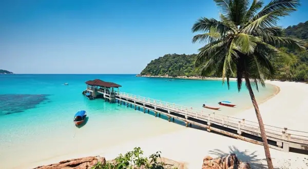 Traumhaftes Malaysia Wetter im Juli: Türkisblaues Meer, weiße Sandstrände, Palmen und eine Anlegestelle mit Booten. Perfekt für einen Urlaub!