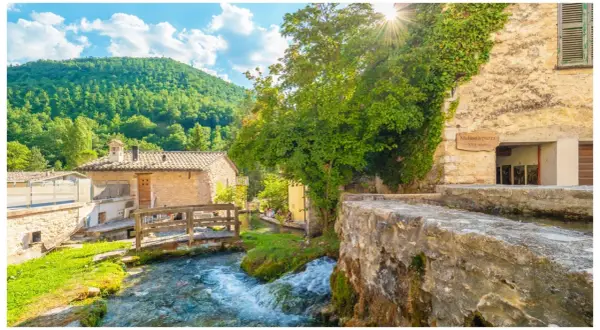 Un ruscello attraversa un borgo umbro con case in pietra e vegetazione lussureggiante. Una cartina ideale per scoprire i borghi dell'Umbria.
