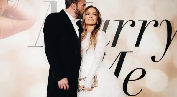 Ben Affleck całuje w czoło Jennifer Lopez, która w białej sukni trzyma torebkę. Para wygląda na zakochanych.