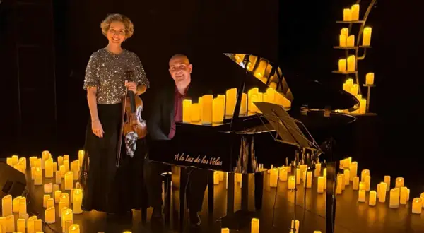 Músicos disfrutan de un concierto con velas. Una violinista y un pianista posan junto a un piano rodeado de velas encendidas.