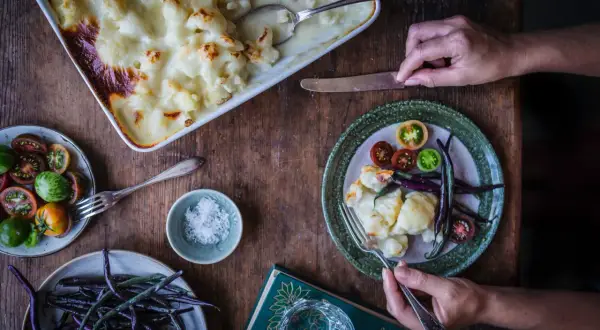 En härlig gratinerad blomkål i en form, serverad med färska grönsaker och en bok.