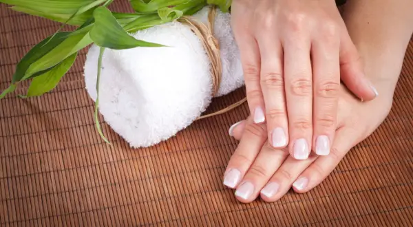 Delikatne dłonie z francuskim manicure, biały ręcznik i zielone liście bambusa. Czy to jest manicure japoński?