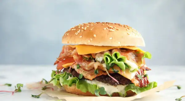Soczysty burger z wołowiny z bekonem, serem i warzywami na jasnym tle.