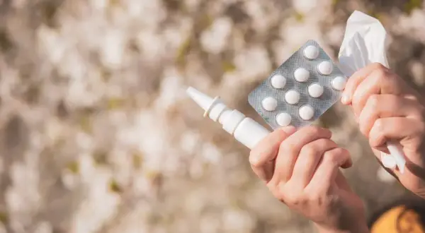 Ręce trzymające spray do nosa, tabletki i chusteczkę, gotowe na walkę z alergią.