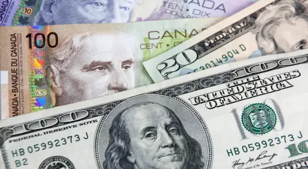 Kanadyjski dolar i amerykańskie banknoty, w tym 100 dolarów kanadyjskich i 100 dolarów amerykańskich, tworzą finansową mozaikę.