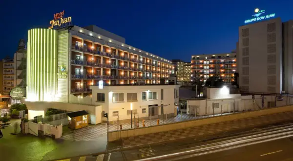 Hotel Don Juan Resort nocą, z neonowym oświetleniem i widokiem na wiele balkonów.