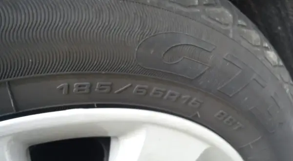 Gros plan sur un pneu rechapé avec inscription 185/65R15. La jante est visible en bas.