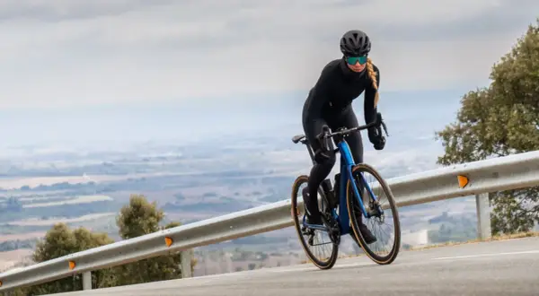 Kobieta w kasku i okularach jedzie na rowerze z niebieskim, aerodynamicznym nadwoziem. Silnik umieszczony centralnie zapewnia moc podczas podjazdu.