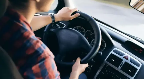 Mężczyzna w kratę prowadzi auto. Zastanawiasz się, co to jest amortyzacja samochodu? To proces zużywania się pojazdu.