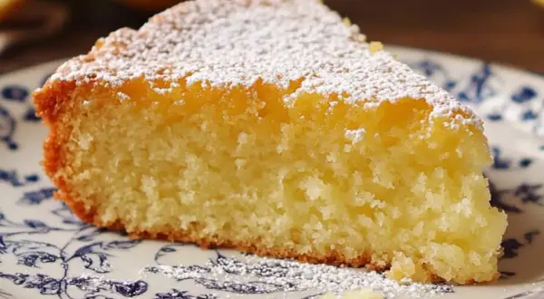 Tranche de fondant citron mascarpone saupoudrée de sucre glace, sur une assiette ornée de motifs bleus.