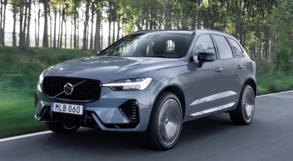 Szary Volvo XC60 z napędem hybrydowym, poruszający się po leśnej drodze. Dostępne różne silniki.
