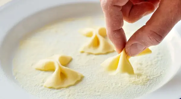 Hand formt Farfalle-Nudeln in einer Schüssel mit Grieß.
