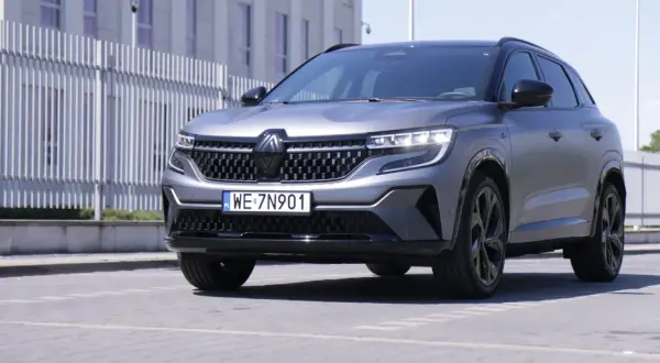 Nowy Renault Austral w matowym, szarym kolorze prezentuje się elegancko na tle nowoczesnego budynku.