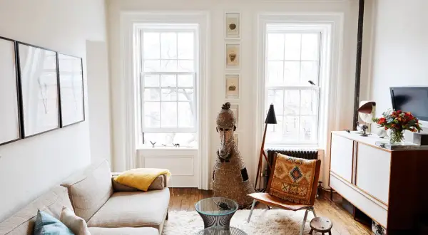 A bright living room with a sofa, fluffy rug, and two windows, demonstrating how to make a small space feel large with light and airy decor.