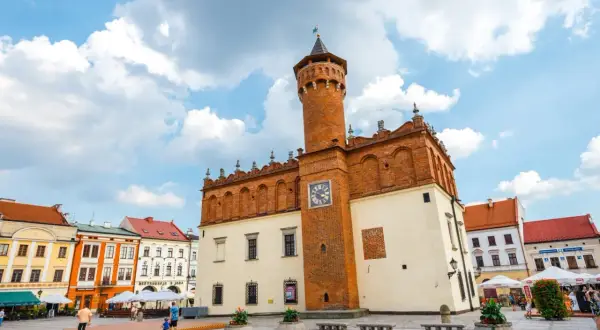 Rynek w Tarnowie z ratuszem i kolorowymi kamienicami. Słoneczny dzień, chmury na niebie.