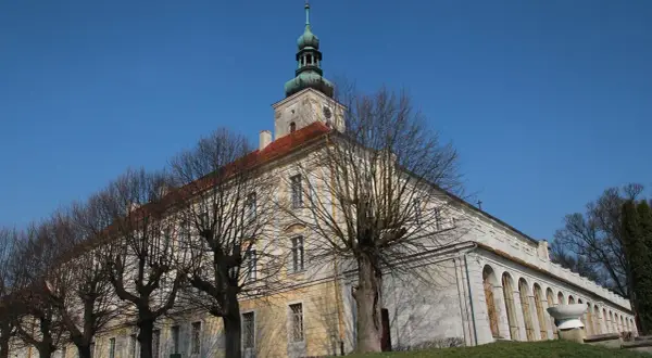 Dawny pałac w Oleśnicy Małej z charakterystyczną wieżą i arkadowym krużgankiem, otoczony nagimi drzewami.