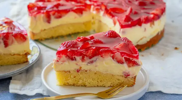 Ein saftiger Erdbeer Schmand Kuchen Springform, mit frischen Erdbeeren und rotem Tortenguss, auf einem Teller mit einer Gabel.