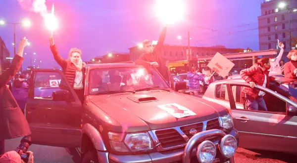 Ludzie z flarami przy samochodach, protestują. Tekst po polsku "Bella Ciao" może być na transparentach.