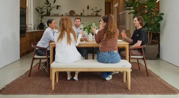 Friends enjoy drinks around a wooden table, showcasing a stylish mix and match of dining chairs and a bench for a relaxed gathering.