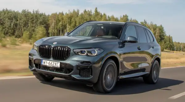 Ciemnozielone BMW X5 45e pędzi po drodze, otoczone zielenią lasów.