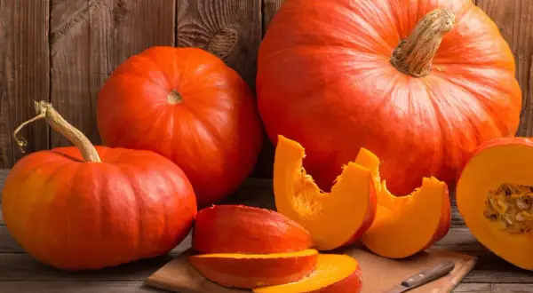 Pomarańczowe dynie, w tym połówka i kawałki na desce, przypominają o bogactwie witamin i minerałów, jakie kryje w sobie dynia.