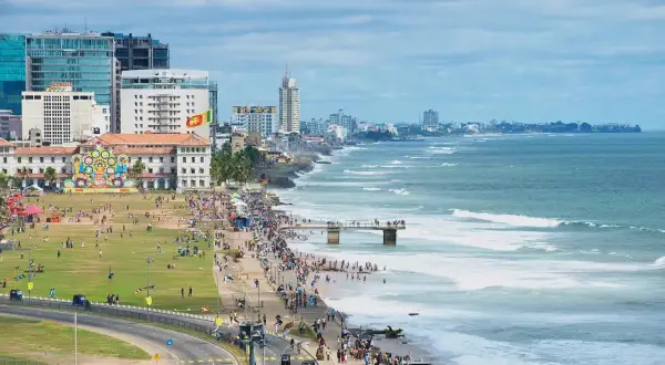 Kolombo, Sri Lanka na własną rękę: tętniące życiem wybrzeże z ludźmi spacerującymi po plaży i zielonym parku, nowoczesne budynki i ocean z falami.