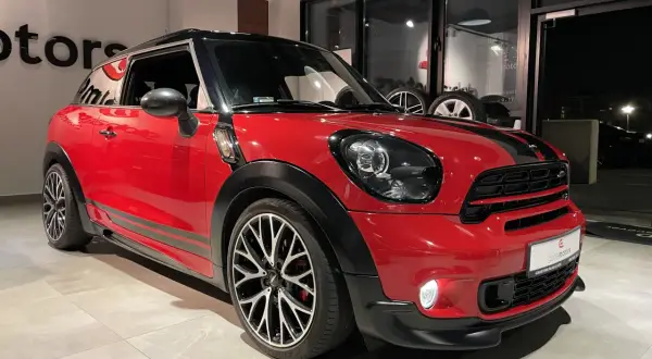Czerwony mini paceman z czarnymi pasami i felgami stoi w salonie.