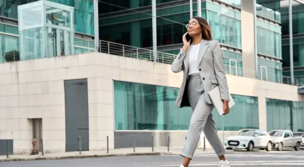 Elegancka kobieta w garniturze, z laptopem pod pachą, rozmawia przez telefon. To kwintesencja mody do pracy w nowoczesnym wydaniu.