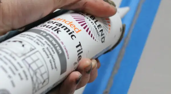 Hand holding a tube of "Sanded Ceramic Caulk" in "19 Pewter" color.
