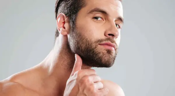 Un homme au regard intense, sa main effleurant sa barbe bien taillée. Une coupe barbe homme parfaite pour un style affirmé.