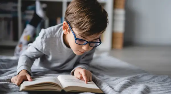 Niño con gafas azules concentrado en un libro abierto, aprendiendo a leer.