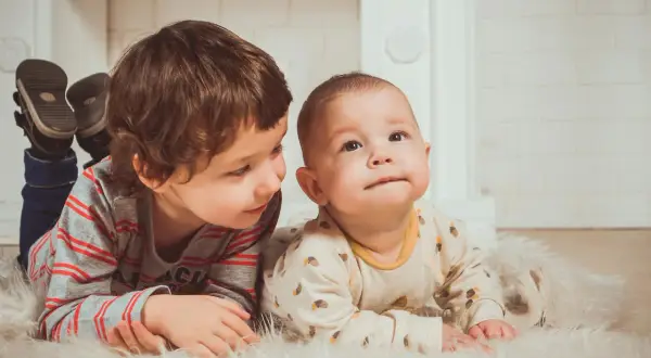 Dwóch braci leży na dywanie. Starszy patrzy na młodszego. Może to przyszli beneficjenci Kinderzuschlag?