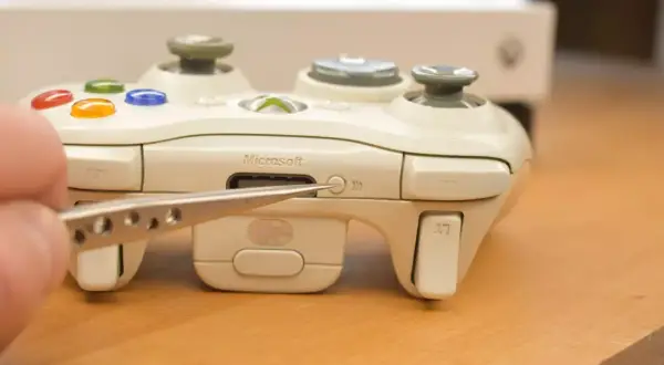 Biały kontroler Xbox z pęsetą wskazującą na przycisk synchronizacji.