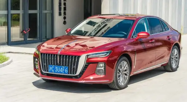 Elegancki, czerwony Hongqi H5 lśni w słońcu przed nowoczesnym budynkiem.