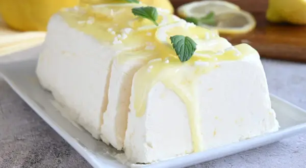 Un delizioso semifreddo al limone, guarnito con scorzette, menta e una glassa gialla, pronto per essere gustato.