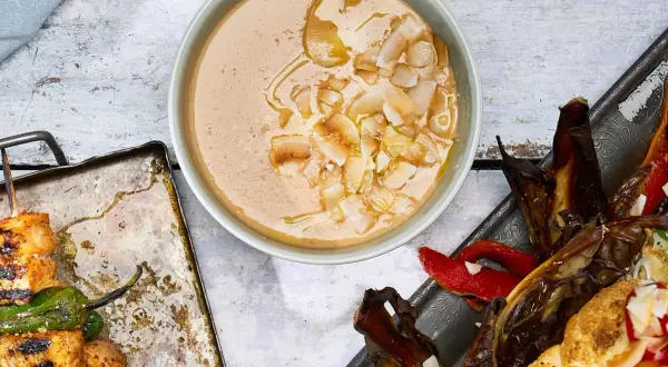 En krämig tahini-sås med kokosflingor, bredvid grillspett med kyckling och grönsaker samt ugnsbakad aubergine och paprika.