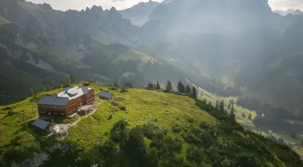 Holzhaus auf einem grünen Hügel, umgeben von majestätischen Bergen. Ein perfekter Ort für die Dachstein Sonnenrunde.