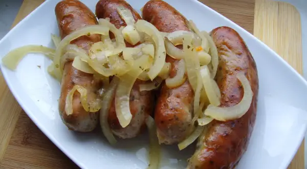 Biała kiełbasa pieczona w cebuli i musztardzie, podana na białym talerzu.