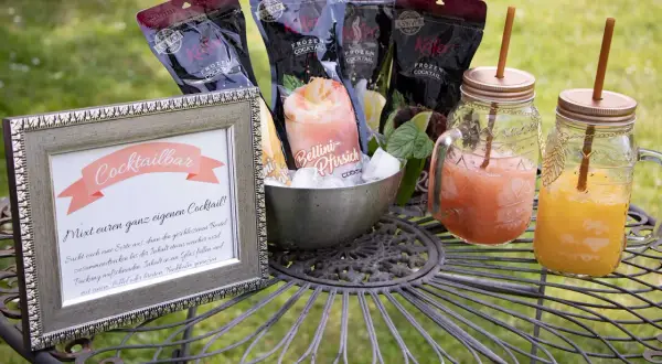 Cocktailbar-Schild und gefrorene Cocktails für eine Hochzeit. Mehrere Beutel mit gefrorenen Cocktails und zwei fertige Getränke in Gläsern mit Strohhalmen.