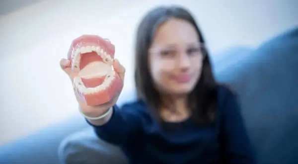 Dziewczynka trzyma model szczęki, pokazując zęby. Może to być związane z edukacją o higienie jamy ustnej, gdzie azotan potasu zastosowanie ma w pastach do zębów.