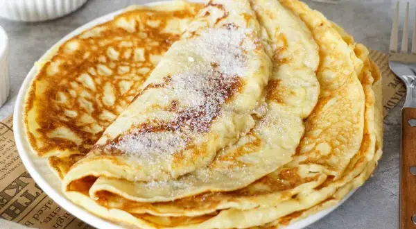Ein Stapel goldbrauner Pfannkuchen, bestreut mit Zucker. Ein einfaches Pfannkuchen Rezept für jeden Tag.