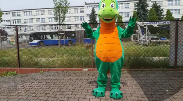 Zielony strój smoka z pomarańczowym brzuchem, stojący na chodniku.