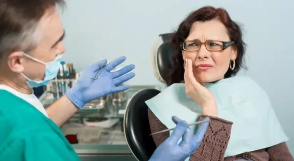 Dentysta wyjaśnia pacjentce, na czym polega zatrucie zęba, która odczuwa silny ból.