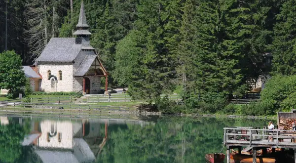 Suggestiva chiesa nel lago trentino, con riflessi sull'acqua verde smeraldo e un pontile in legno con barche.